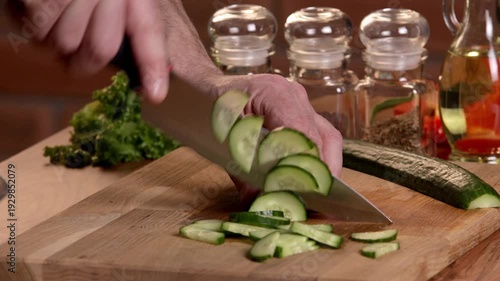A cook cuts cucumber into pieces for a salad with a knife.