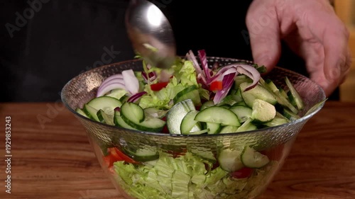 The cook mixes a salad of cucumber, pepper and lettuce leaves in a bowl.