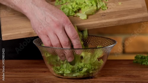 A male chef transfers green salad leaves from a cutting board into a bowl