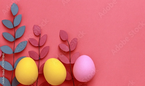 Colorful Easter eggs and paper leaves arranged on a pink background with copy space.
