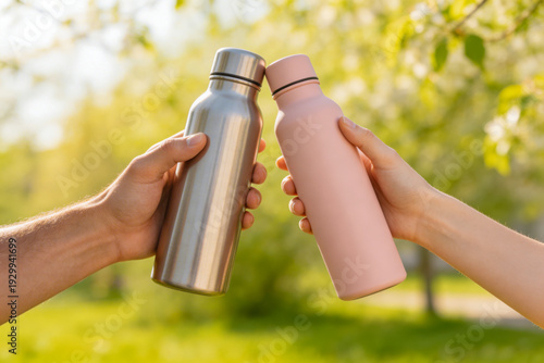 Two people clinking reusable water bottles outdoors in sunlight