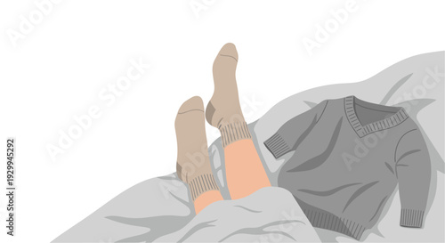 A pair of light brown-skinned legs wearing beige socks protrudes from under a light gray blanket, next to a folded gray V-neck sweater.