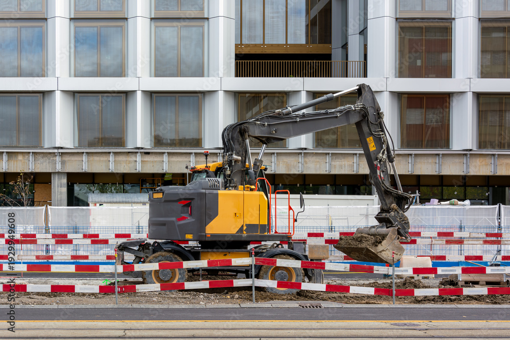 Obraz premium Excavator at urban construction site with safety barriers