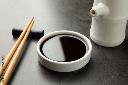 Soy sauce in bowl and chopsticks on grey table, closeup