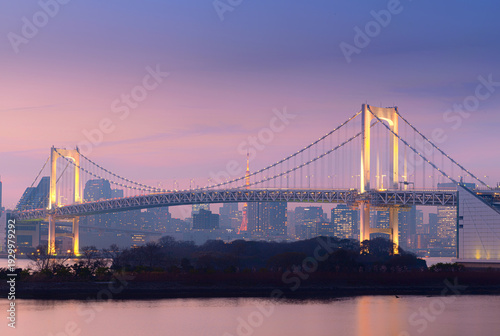 Tokyo, Japan – Evening cityscape featuring Rainbow Bridge illuminated over Tokyo Bay with Tokyo Tower visible in the background, showcasing modern skyline and urban architecture at dusk in Tokyo, 