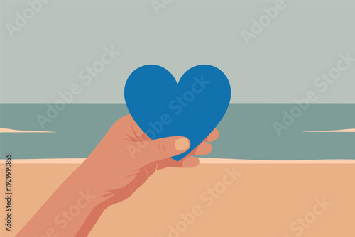 Hand holding blue heart on beach with ocean view
