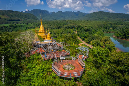 Aerial drone view of golden pagoda at Wat Prangkasi in Thong Pha Phum, Kanchanaburi, Thailand surrounded by lush forest mountain landscape