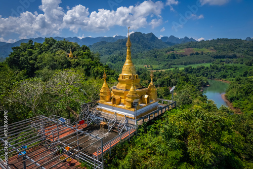 Aerial drone view of golden pagoda at Wat Prangkasi in Thong Pha Phum, Kanchanaburi, Thailand surrounded by lush forest mountain landscape