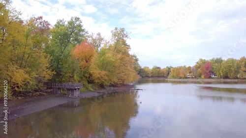 Moving slowly above water, flying away from wild geese in the Fall, surrounded by colorful trees