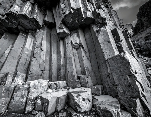 Geometric rock columns ascend, a textured grayscale landscape. Sunlight highlights the rough, fractured formations, revealing a majestic display