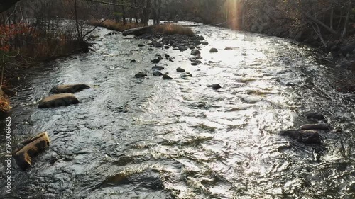 Drone flying at low altitude over the rivers with rapids getting closer to a small island in the Fall