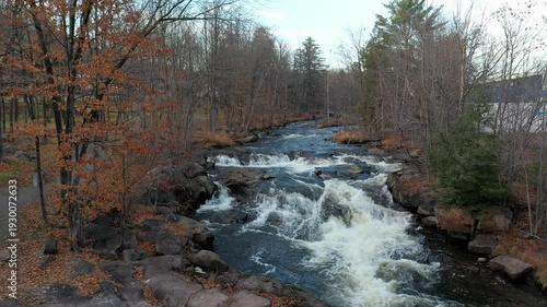 Drone flying mid-air over the rivers with rapids staying still over the small waterfalls with colorful trees in the Fall