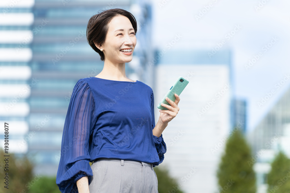 Fototapeta premium ビル街でスマートフォンを操作している女性