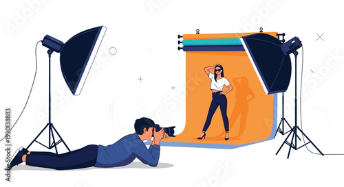 Professional photographer lying on the floor taking a photo of a female model posing in a studio with lighting equipment.