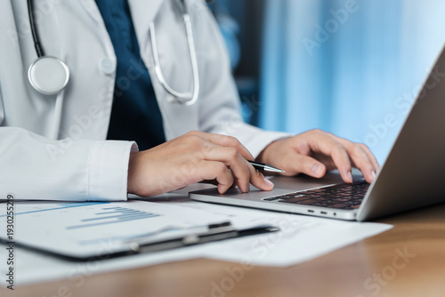 The doctor is taking notes, recording patient information in the hospital examination room. working on a laptop computer iagnosis, treatment, and professional medical service.
