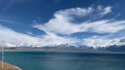 A stunning view of Namtso Lake in Tibet sits beneath the towering Nyainqêntanglha mountains, bright, clear, and breathtaking.