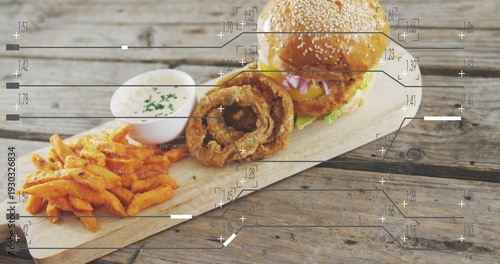 Displaying sesame-seed cheeseburger, onion rings, sweet-potato fries and ramekin on weathered board