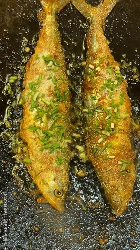 Crispy fried fish with green onions in a sizzling pan