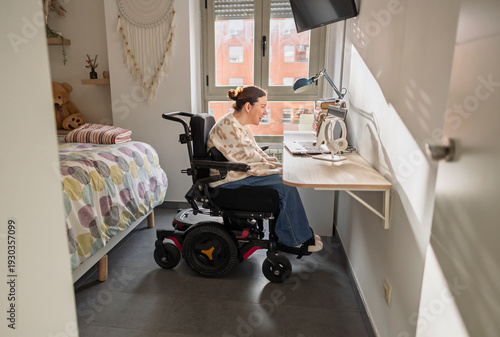 Canvas-taulu Young woman using electric wheelchair working from home