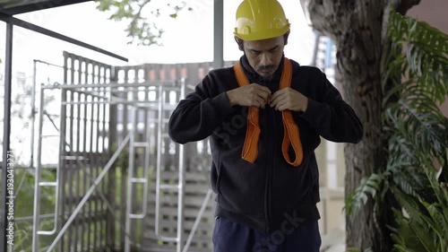Worker Fastening Harness In The Work Site, A focused worker securing a safety harness on site, highlighting professional safety standards, perfect for industrial, safety awareness and documentary.