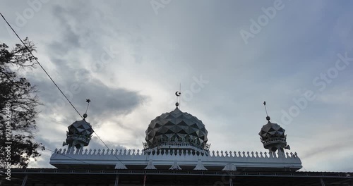 Islamic mosque with three domes against cloudy sky.
