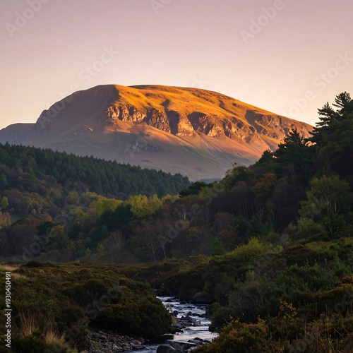 Mountain peak bathed in golden sunset light, overlooking a valley with a stream