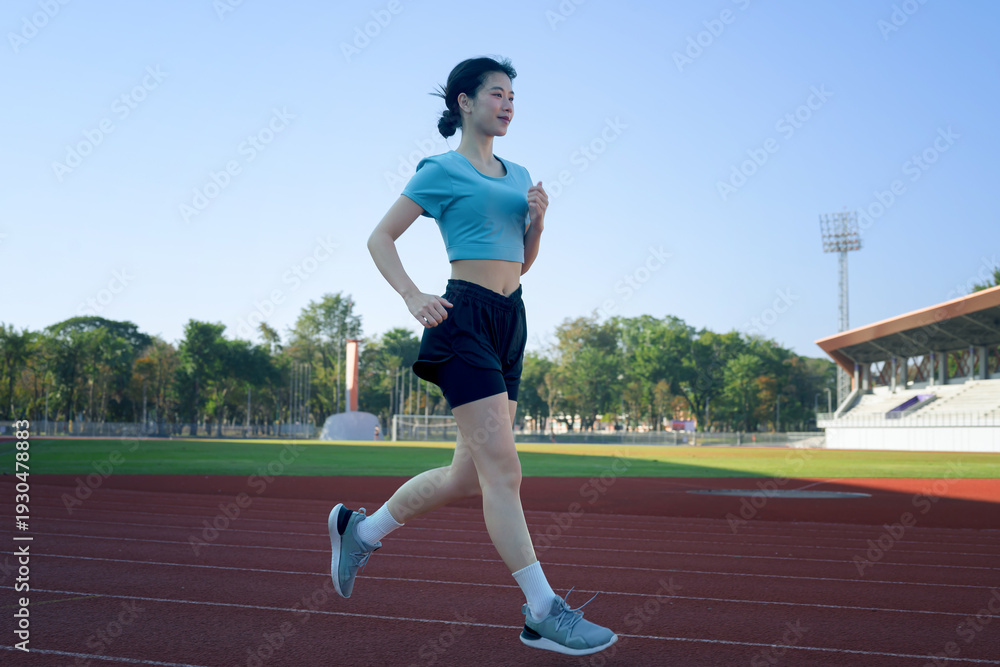 Obraz premium Young Asian woman jogging on outdoor running track at stadium, morning exercise