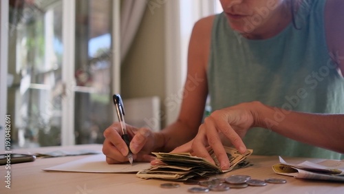 Принти на полотні Woman at home counting cash and coins at a table, writing notes with a pen while