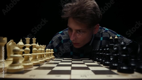 A young man is sitting in front of a chessboard with pieces and thinking about the next move. The chess player is assessing the risks before making the first move. A thoughtful chess player