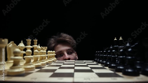 A young man looks out from under the chessboard, thinking about his first move, and then hides under the table.