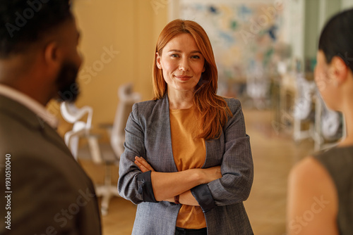 Portrait of confident businesswoman with arms crossed listening to diverse colleagues in corporate meeting