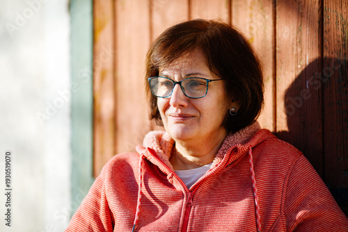 Mature caucasian woman outdoors with glasses and red jacket in sunlight
