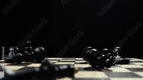 Black chess pieces on a board stand in a row. A man's hand knocks down the pieces on a chessboard on a black background 4к
