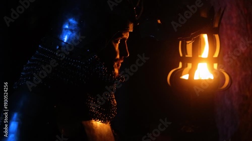 A knight in full armor, holding a sword and torch, stands in a dark night forest. A medieval warrior searches in the darkness.