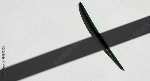 A dramatic overhead perspective captures the stark contrast of a sharp, elongated shadow cast onto a clean, minimalist white surface, wall, blank, horizontal