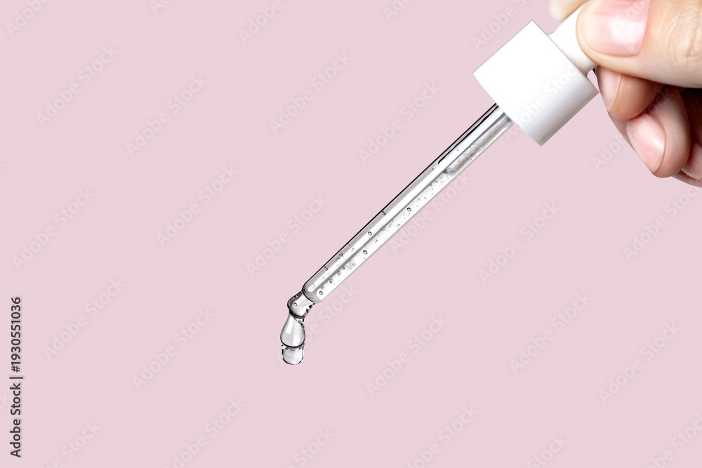 Fototapeta premium Pipette with serum in hand. Drips drop isolated on pink background, copy space photo close up