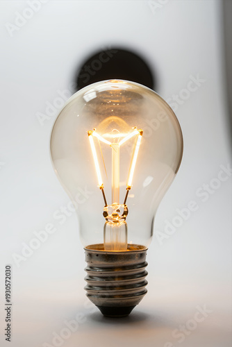 Wallpaper Mural Vintage Filament Light Bulb Glowing Warmly with Visible Glass and Metal Base Against Soft White Background for Creative Lighting or Design Projects Torontodigital.ca