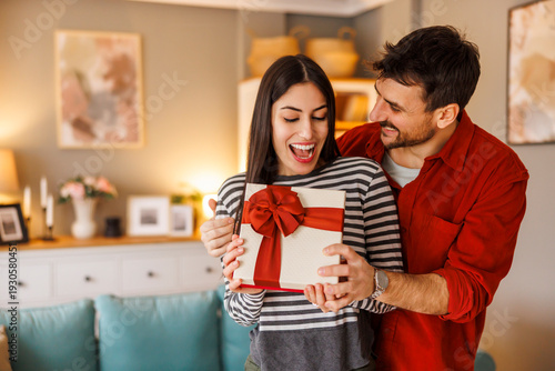 Man surprising woman with a gift while spending couple's time together at home