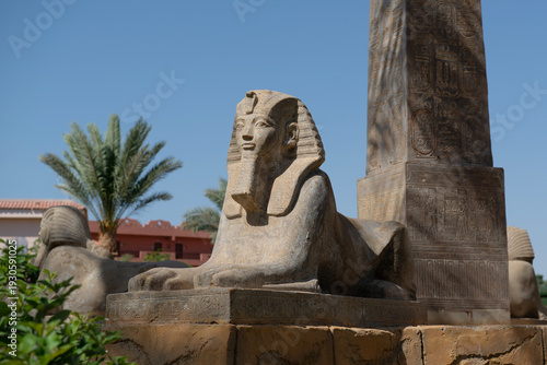 Ancient Egyptian Sphinx Statue with Hieroglyphic Obelisk Under Blue Sky