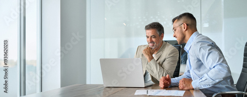 Quadro em tela Happy busy professional team of two business men executive having discussion, male partners working using laptop looking at computer analyzing online tech data at work in office sitting at desk