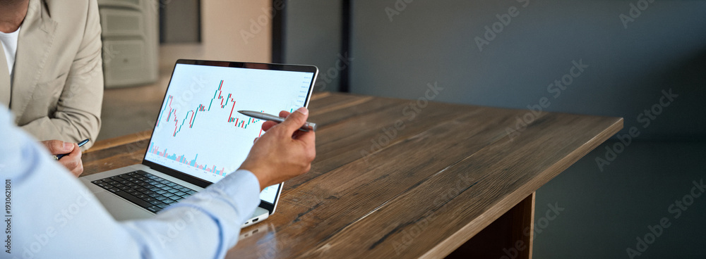 Naklejka premium Financial advisor explaining invest stock market data consulting investor. Two business men analysts doing finance trading analysis pointing at chart on laptop screen working in office. Close up.