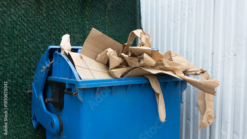 Photos Overfilled blue recycling bin with brown cardboard waste and paper packaging