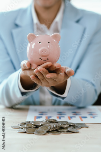 Business professional holding a pink piggy bank above stacked coins on a desk, symbolizing savings growth, financial planning, investment strategy, and long-term wealth management.