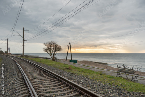 Railway tracks running along Black Sea shoreline in Abkhazia under cloudy sky with power lines, coastal landscape, Transport infrastructure scene suitable for logistics marketing, regional promotion