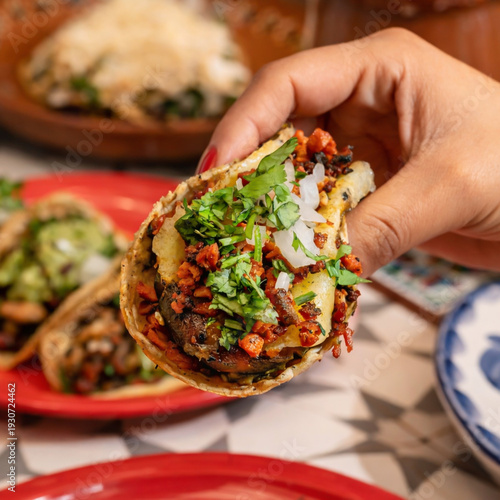 Mano sosteniendo taco de pastor con cilantro y cebolla 