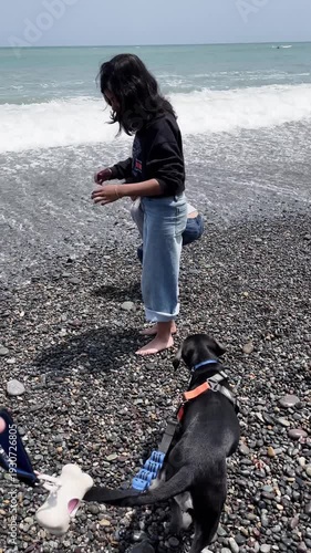 Sisters playing with puppy on pebble beach with ocean waves