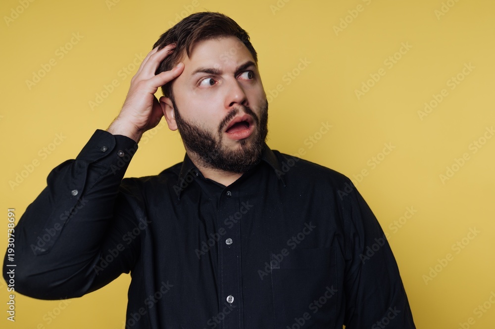 Obraz premium Surprised man on vibrant yellow background expresses shock with open mouth and hand on head, capturing a moment of disbelief