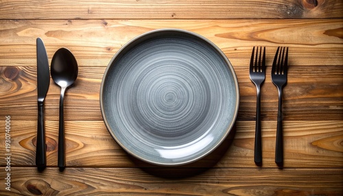 Neutral overhead table setting with gray plate, black cutlery on weathered wood background