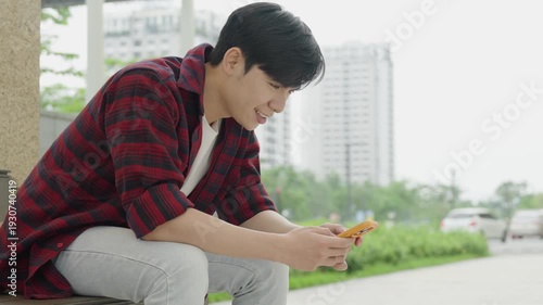 young Asian man absorbed in his phone in an urban setting