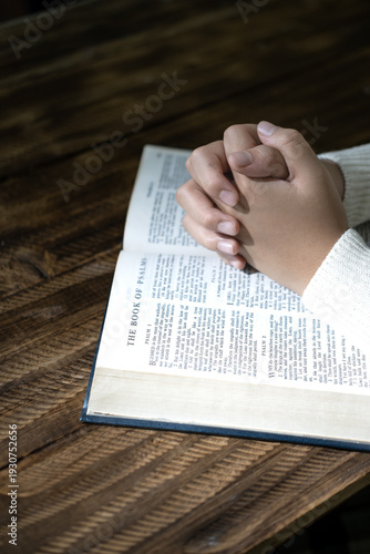 Praying Hands Over Open Bible – Christian Faith and Worship Concept. Close-up of hands clasped in prayer over an open Bible. Spiritual devotion, Christian faith, hope, and religious reflection